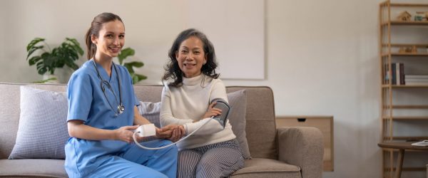 Happy senior woman having her blood pressure measured in a nursing home by her caregiver. Happy nurse measuring blood pressure of a senior woman in living room..